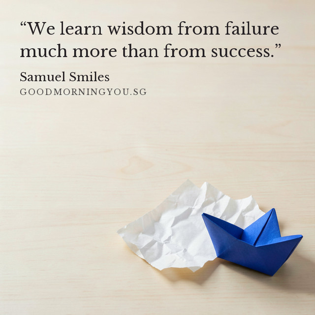 A blue folded paper boat beside a crumpled sheet on pale timber. “We learn wisdom from failure much more than from success.” — Samuel Smiles