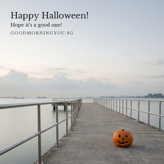 A carved jack-o'-lantern on a long concrete jetty with metal railings stretching out over a calm grey sea at dawn, and the words "Happy Halloween! Hope it's a good one!"