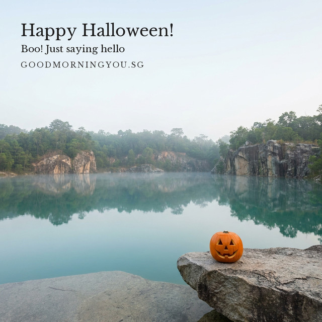A carved jack-o'-lantern on a rock at the edge of a misty turquoise quarry lake ringed by cliffs and forest, and the words "Happy Halloween! Boo! Just saying hello"